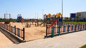 A playground with various play structures, a fenced area, and a paved walkway. - Beautiful pool view apartment in Ola Blanca 4533 (Sidi Rahal)