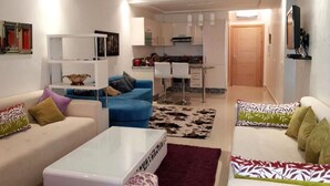A modern living room with a sofa, a coffee table, and a kitchen in the background. - Beautiful pool view apartment in Ola Blanca 4533 (Sidi Rahal)
