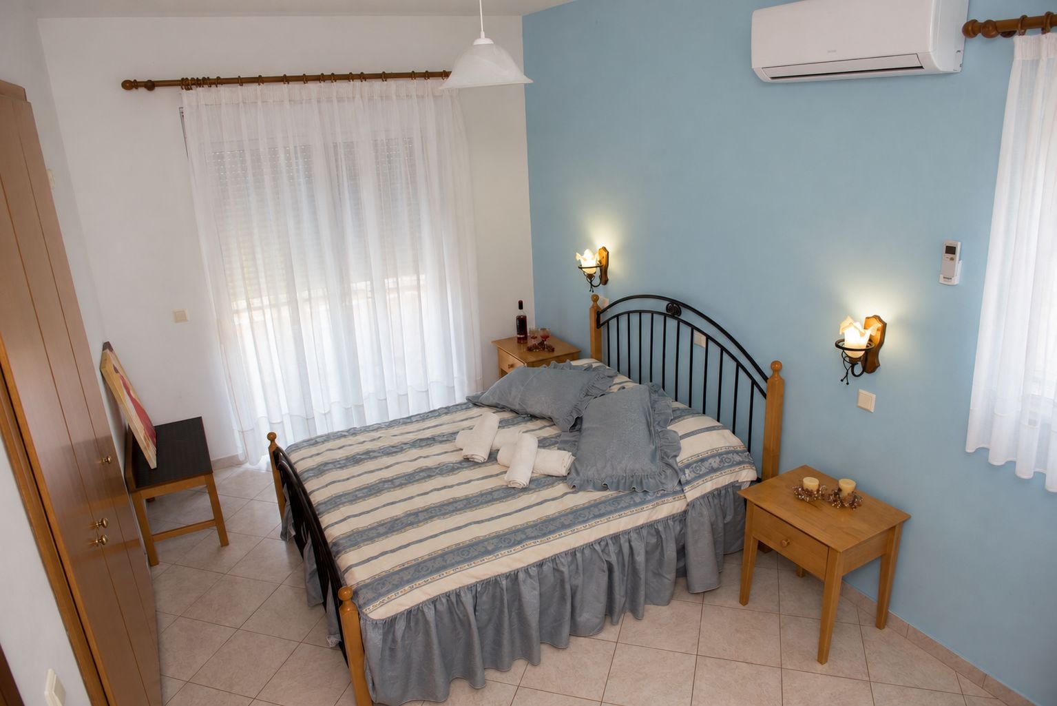 A bedroom with a bed, a nightstand, a wall-mounted lamp, and an air conditioning unit.