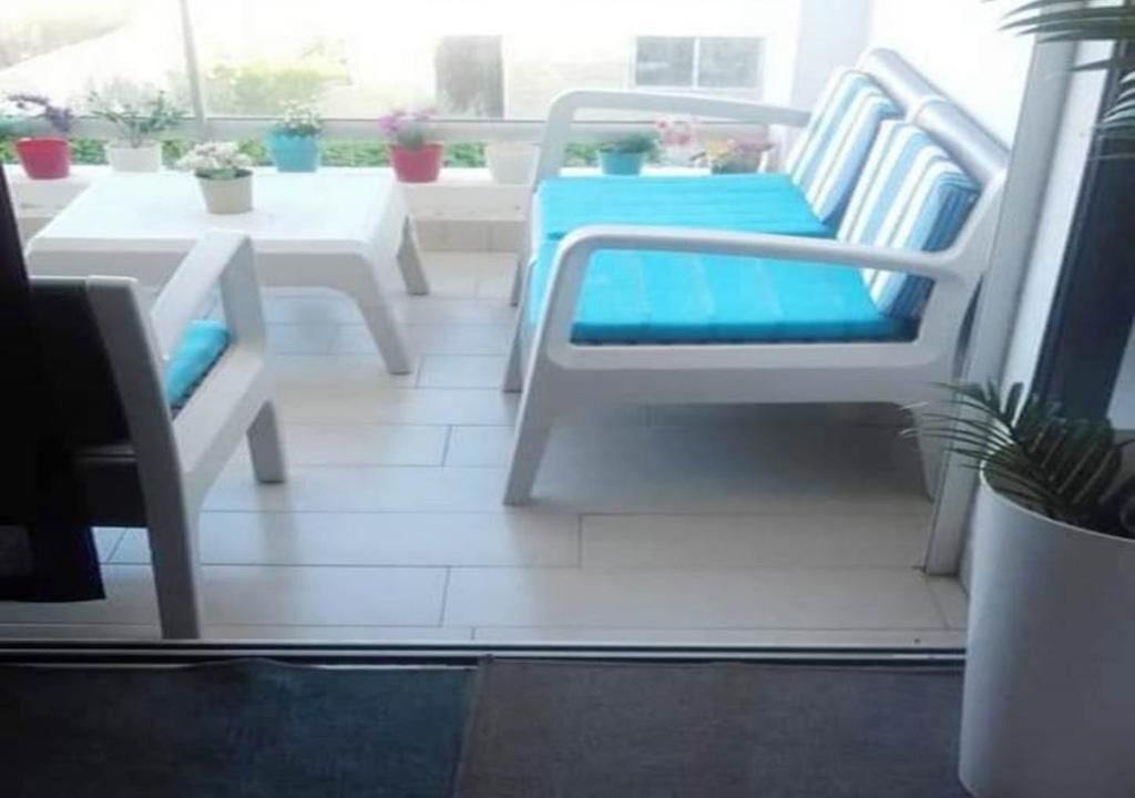 A patio area with a white sofa and a table, surrounded by potted plants.