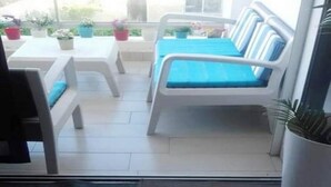 A patio area with a white sofa and a table, surrounded by potted plants. - Very Nice apartment in Eden Tamaris 4175 (Dar Bouazza)
