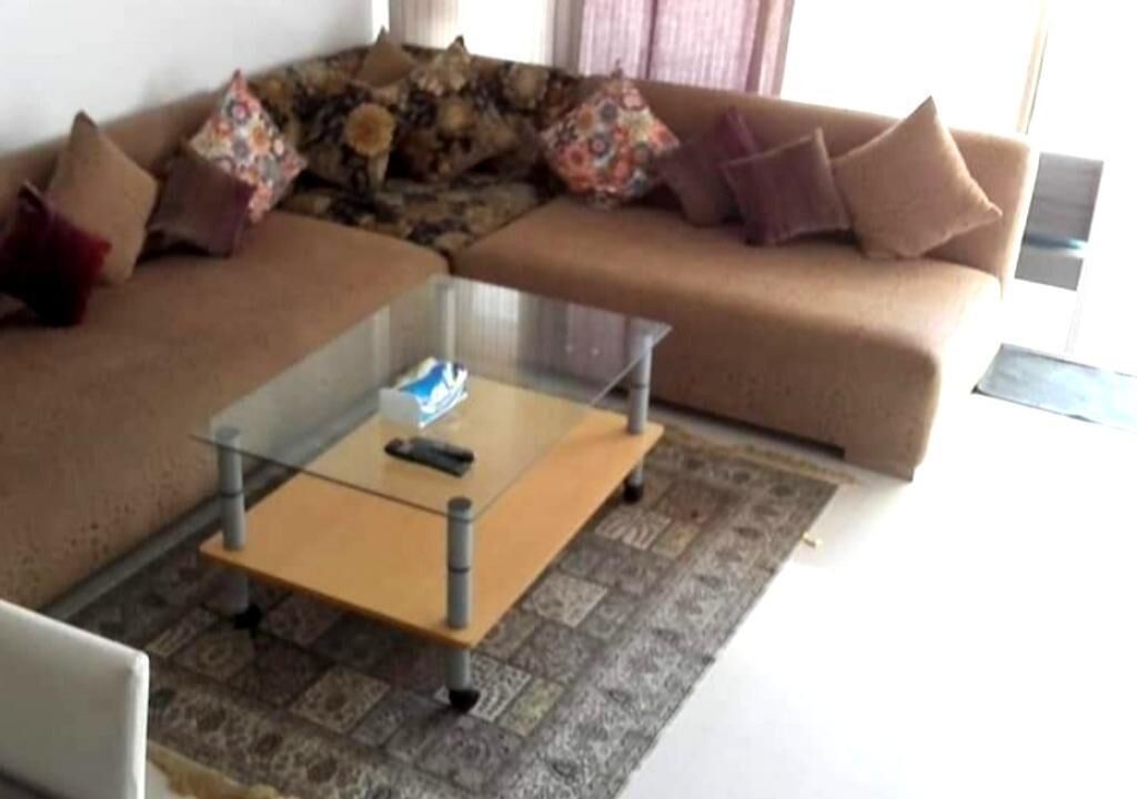 A living room with a sofa, a glass-top coffee table, and a patterned rug.