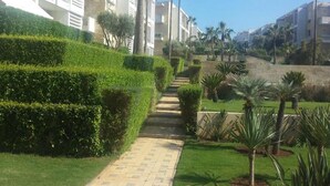 A pathway leading to a building with multiple balconies, surrounded by well-maintained greenery and palm trees. - Very Nice apartment in Eden Tamaris 4175 (Dar Bouazza)