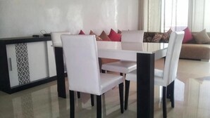 A dining area with a white table and chairs, a sofa with patterned cushions, and a cabinet with a patterned design. - Very Nice apartment in Eden Tamaris 4175 (Dar Bouazza)