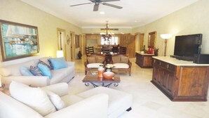 Amplia sala de estar con un sofá blanco, una zona de comedor con muebles de madera, un televisor y una araña.