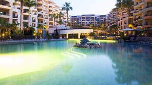 Una piscina de hotel con fuente, palmeras y un edificio de varios pisos al fondo.