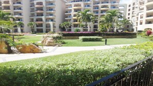 Un hotel con varios balcones, un jardín bien cuidado con palmeras y un sendero.