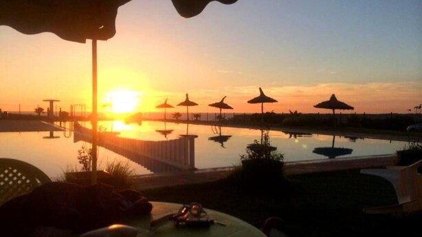 Een zonsondergang boven een zwembad met parasols en ligbedden.