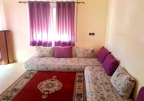 Ein Wohnzimmer mit einer Sofagarnitur, einem gemusterten Teppich und violetten Vorhängen.