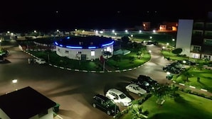 Een rond gebouw met een blauw verlichte bovenkant, omgeven door een parkeerplaats en begroeiing.