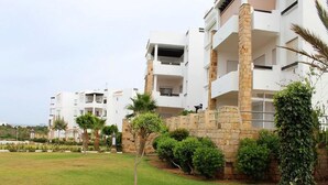 Un immeuble d’appartements moderne doté de nombreux balcons, de piliers en pierre et d’une pelouse bien entretenue.