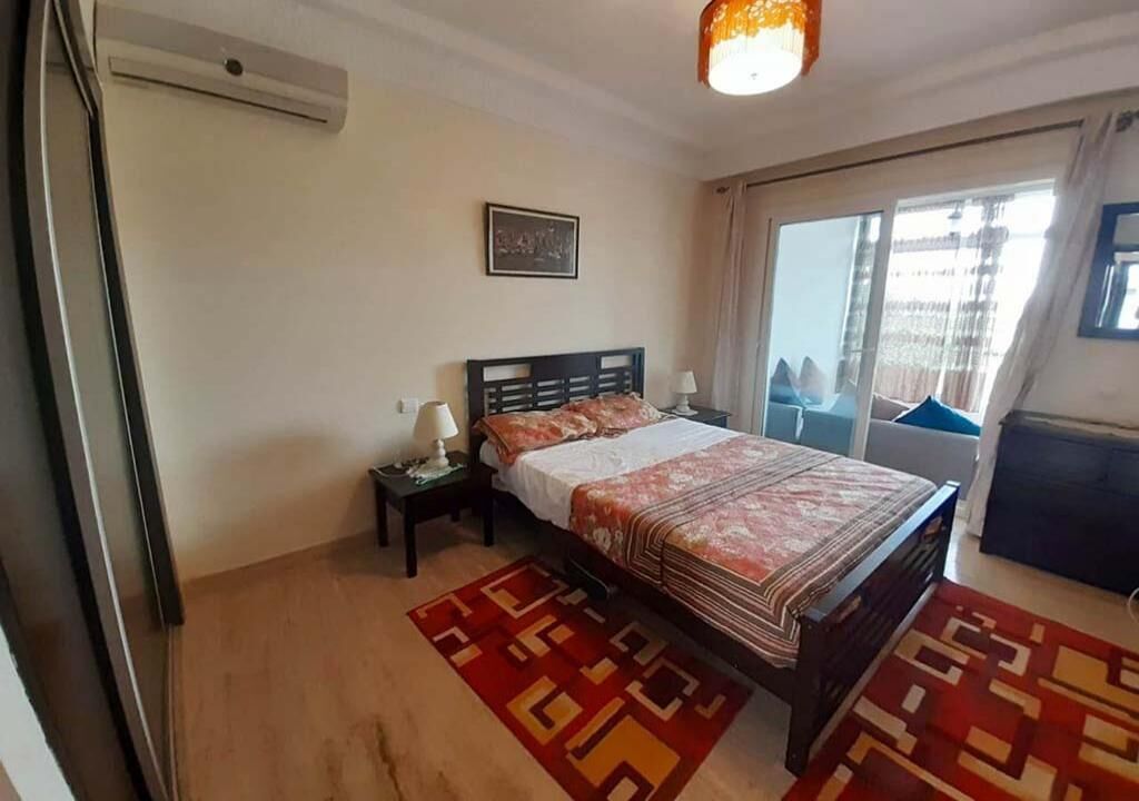 Un dormitorio con cama, mesitas de noche, una ventana con cortinas y vistas al exterior.
