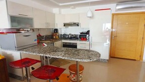 A modern kitchen with white cabinets, a granite countertop, and red bar stools. - Wonderful apartment in Ola Blanca 4517 (Sidi Rahal)