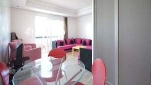 A modern living room with a glass table and red chairs, a pink sofa with black cushions, and a sliding glass door leading to a balcony. - Beautiful Studio in Playa Del Pacha 4429 (Mdiq)