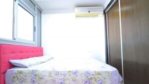 A bed with a floral bedspread, a pink headboard, and a window with blinds. - Beautiful Studio in Playa Del Pacha 4429 (Mdiq)