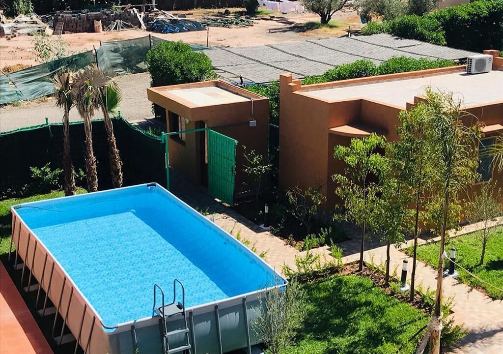 A rectangular swimming pool with a ladder, surrounded by greenery and buildings.