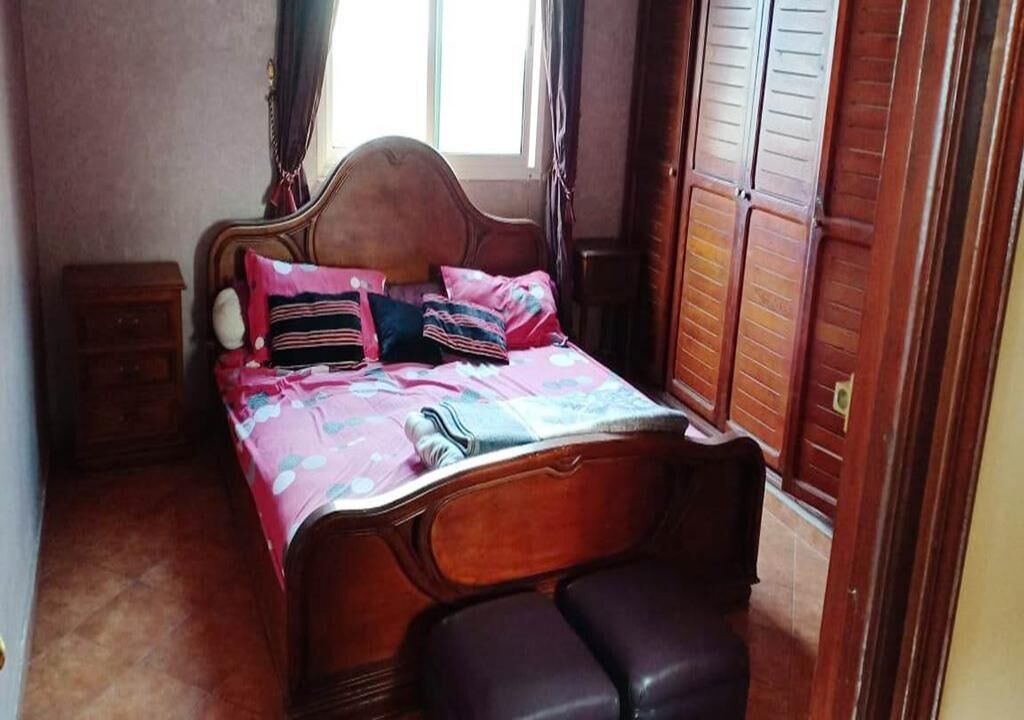 Un dormitorio con una cama de madera, una mesita de noche y un ventanal con cortinas.