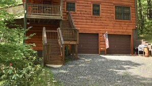 A two-story log cabin with a balcony, a garage, and a gravel driveway.