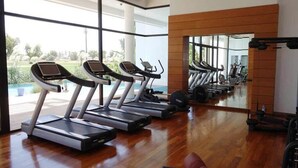 Une salle de sport équipée de tapis de course, d’appareils de musculation et d’un grand miroir.