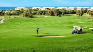 Un parcours de golf offrant une vue dégagée sur l’océan, avec une rangée de maisons de plage en arrière-plan.