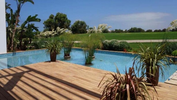 Une terrasse en bois avec une piscine, entourée de différentes plantes et arbres.