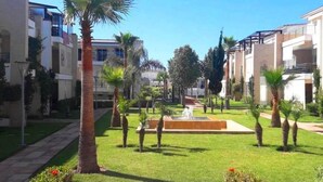 Un patio central con una fuente, rodeado de palmeras y césped cuidado.