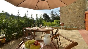 An outdoor dining area with a table set for two, a wooden chair, a fruit plate, a pitcher, and a large umbrella. -  YOUR EXCLUSIVE HOLIDAY BETWEEN VINEYARDS AND CASTLES (Villa A Sesta)