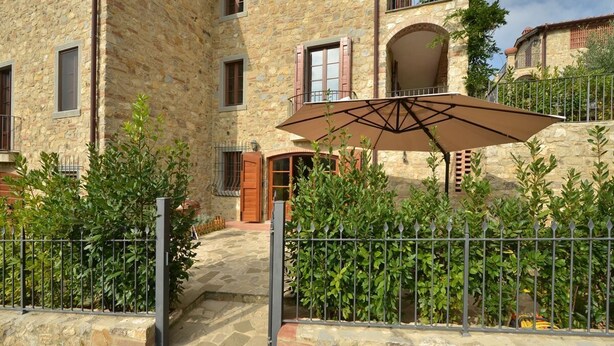 A stone building with a central entrance, a metal fence, and a large umbrella. -  YOUR EXCLUSIVE HOLIDAY BETWEEN VINEYARDS AND CASTLES (Villa A Sesta)