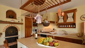 A kitchen with a central island, a brick oven, hanging baskets, and a clock on the wall. -  YOUR EXCLUSIVE HOLIDAY BETWEEN VINEYARDS AND CASTLES (Villa A Sesta)
