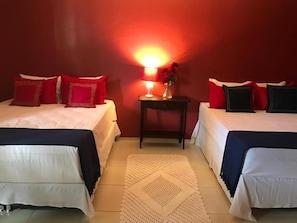 A hotel room with two beds, a nightstand with a lamp, and a decorative vase. - Suites Bouganville 2 (Ipojuca)
