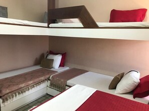 Ein Mehrbettzimmer mit einem Etagenbett und einem Einzelbett. Auf den Betten liegen Kissen und eine Decke.