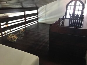 Ein Zimmer mit dunklem Holzboden, einem weißen Sofa, einem kleinen Tisch mit Blumen und einem Fenster mit Blick nach draußen.