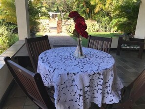Ein runder Tisch mit einer Spitzenleinentischdecke, umgeben von Holzstühlen, draußen mit Blick auf einen Garten.