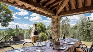 An outdoor dining area with a stone oven, a table set for two with wine glasses and plates, and a view of the countryside. - Villa Bellaria, in the heart of Tuscany (Lucignano)