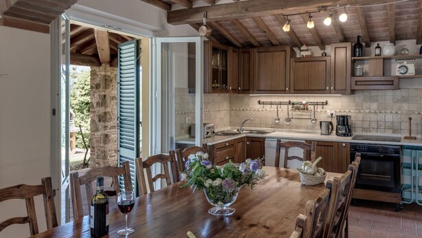 A rustic kitchen with wooden cabinets, a dining table with chairs, and a built-in oven. - Villa Bellaria, in the heart of Tuscany (Lucignano)