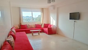 Uma sala de estar espaçosa com um sofá vermelho, uma mesa de centro e uma televisão de tela plana na parede.