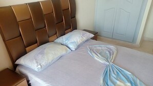 Cama bem arrumada com cabeceira marrom, travesseiro branco e toalha dobrada sobre a cama.
