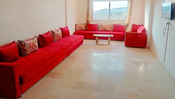 Uma sala de estar espaçosa com sofá vermelho, mesinha de centro e televisão na parede.
