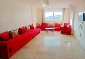 A spacious living room with a red sofa set, a coffee table, and a TV mounted on the wall. - Beautiful apartment in the heart of Marrakech 4425 (Marrakech)