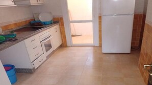 A kitchen with a stove, oven, and white refrigerator. There is a blue bucket and a white door leading to a balcony. - Apartment in Saidia 4305 (Saidia)