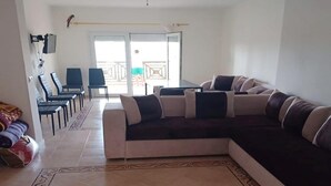 A living room with a sectional sofa, a TV mounted on the wall, and a balcony with a view. - Apartment in Saidia 4305 (Saidia)