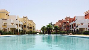 A swimming pool surrounded by multi-story buildings with balconies and palm trees. - Apartment in Saidia 4305 (Saidia)