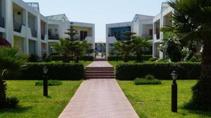 A pathway leading to a building with a symmetrical design, surrounded by well-maintained greenery and palm trees. - Apartment foot in the water in Sary beach 3958 (Sidi Rahal)