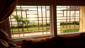 Habitación con sofá orientado a una ventana con barrotes, una cortina cubriendo parcialmente la ventana y vistas a un jardín exterior.