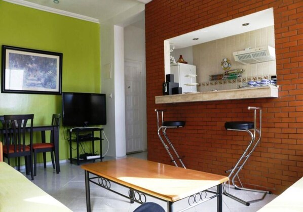 Un salon comprenant un téléviseur, une table à manger et deux chaises. Il y a également un coin cuisine avec un four à micro-ondes et un évier.