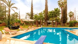A rectangular swimming pool with a blue deck, surrounded by palm trees and lounge chairs.