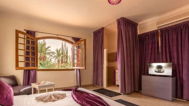 A hotel room with a bed, a TV, a desk, and a window with curtains.