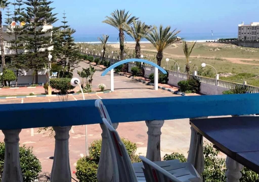 Un balcó amb vista a una zona d'aparcament, palmeres i un edifici al fons.