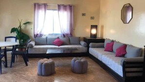 Una sala de estar con un sofá, otomanas, una mesa de comedor y una planta en maceta.