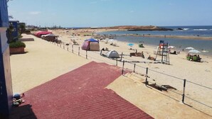 Una playa con un sendero rojo que lleva al agua, sombrillas y sillas.